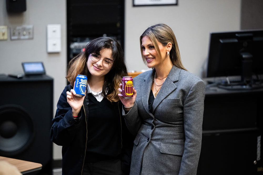 Allison Ellsworth and a UNT student pose for a picture with cans of poppi soda.
